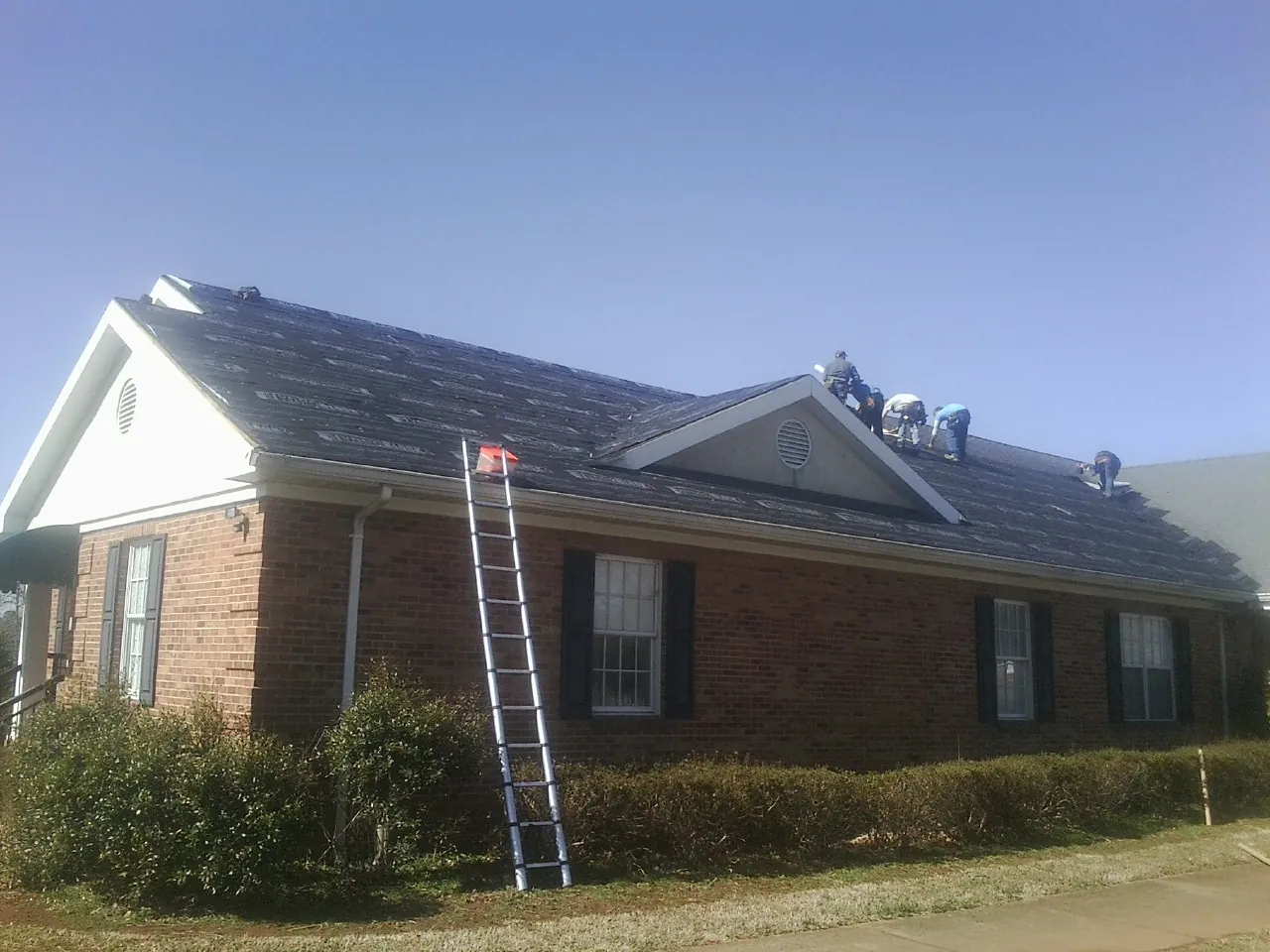 Crew tearing shingles off a brick ranch roof with a ladder set — Emergency Roof Repair work by our crew in El Cerrito