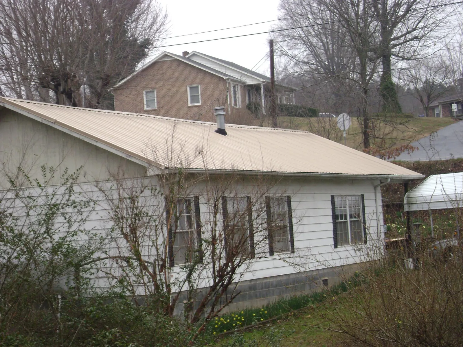 Tan metal roof on a white sided house set into a hillside — Commercial Roofing by Roofing Brothers in El Cerrito